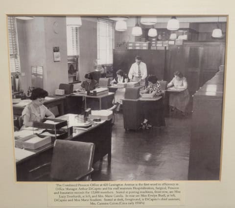 Office staff working at desks in a vintage office setting.