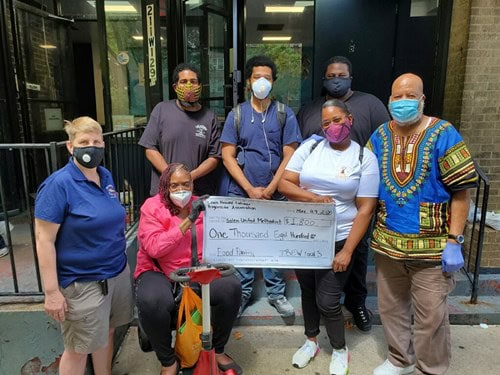 Group of diverse workers holding a donation check outside the JBIE building.